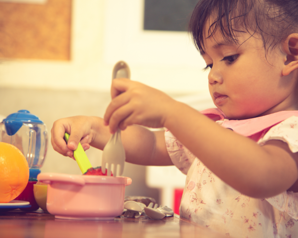 toddler using a fork and spoon to eat at the table